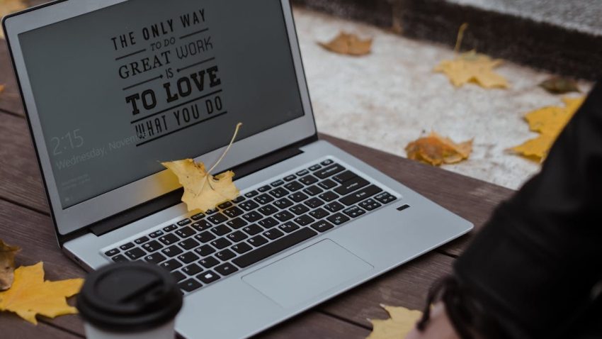 A laptop with inspiring text on screen surrounded by autumn leaves and coffee on a wooden table.